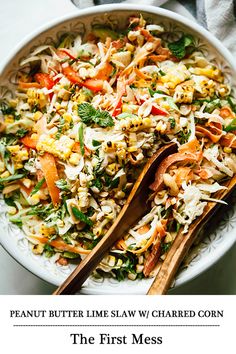 a white bowl filled with salad next to two wooden spoons on top of a table