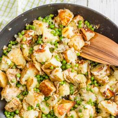 a pan filled with potatoes and peas next to a wooden spoon