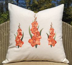 a white pillow with orange flowers on it sitting on a wicker chair in front of some trees