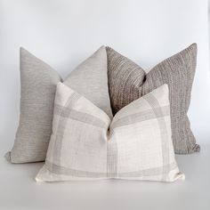 three pillows sitting next to each other on top of a white table with a black and gray checkered pillow