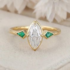 a white diamond and green emerald engagement ring on top of a cushioned surface with flowers in the background