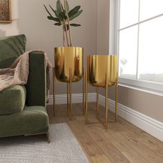 three gold vases sitting next to each other on a green couch in front of a window