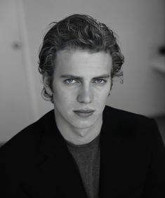 a black and white photo of a man with curly hair wearing a blazer looking at the camera