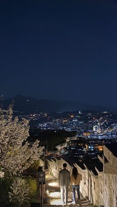 two people are walking up some stairs at night with the city lights in the background