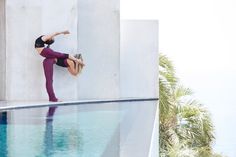 a woman doing a handstand on the edge of a swimming pool with palm trees in the background