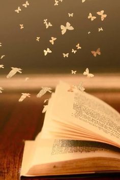 an open book sitting on top of a wooden table with butterflies flying out of it