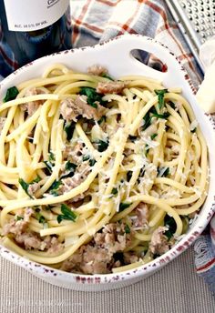 pasta with meat and spinach in a white bowl next to a bottle of wine