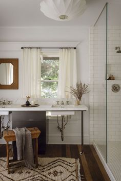 a bathroom with two sinks, a shower and a rug in front of the window