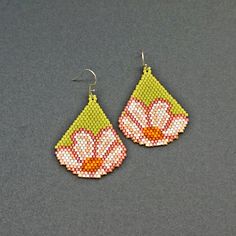 a pair of beaded earrings with pink flowers on green and white tears, sitting on a gray surface