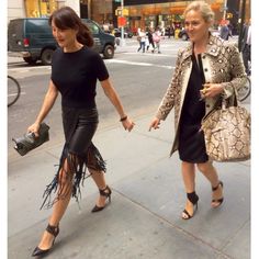 two women are walking down the street holding hands and one is carrying a handbag