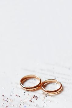 two gold wedding rings sitting on top of a piece of paper covered in confetti