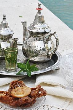 an assortment of tea and pastries on a silver tray next to a swimming pool