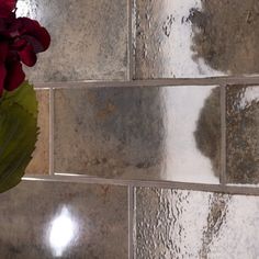 a vase filled with red flowers sitting on top of a tiled wall next to a mirror