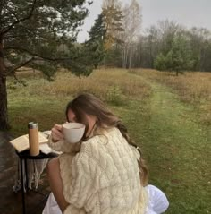 a woman sitting at a table with a cup of coffee in her lap and looking out into the distance