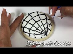 someone is decorating a cookie with white icing and black spider webs on it