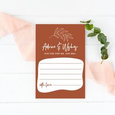 a brown and white wedding stationery with greenery on the top, next to a pink ribbon