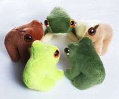 four stuffed animals are arranged in a circle on a white surface, one is green and the other is brown