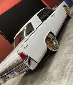 an old white car parked in a garage next to a red wall and black door