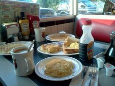 two plates of breakfast food on a table in a diner's dining room with a view of the street