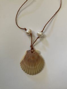 a necklace with a shell and pearls hanging from it's cord on a white surface