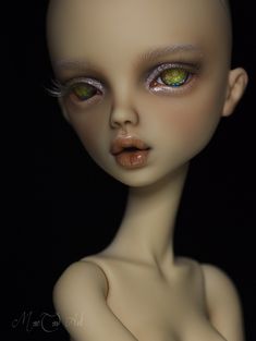 an alien doll with green eyes and white skin is posed in front of a black background