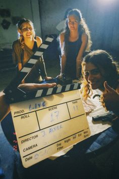 three women sitting around a movie clapper with one pointing at the camera and the other giving thumbs up