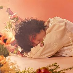 a woman laying on top of a bed next to flowers and plants in a room