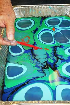 a person is painting an art project with blue and green paint on metal pans