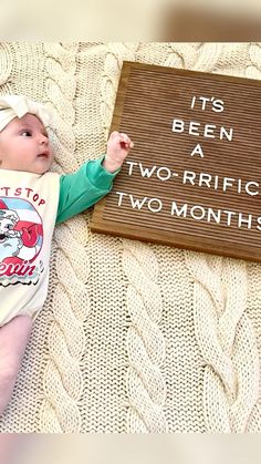 a baby laying on top of a bed next to a sign