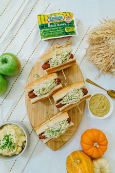 several hot dogs on buns with toppings next to pumpkins and other foods