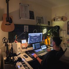 a man sitting in front of a computer desk with music equipment on it and a guitar