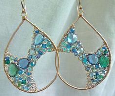 a pair of gold earrings with blue and green stones on the inside are hanging from wire