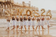 a group of women standing on top of a beach next to the ocean holding up letters