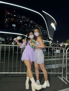 two young women wearing face masks standing next to each other in front of a fence