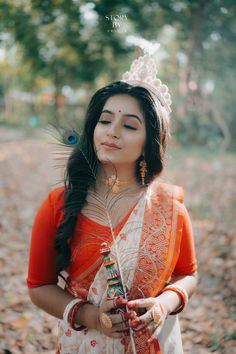 a woman in an orange and white sari with feathers on her head holding a stick