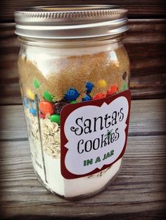 a jar filled with sand and candy on top of a wooden table next to a sign that says santa's cookies mix & bake