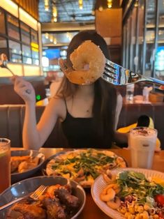 a woman sitting at a table with plates of food in front of her and a fork sticking out of her face