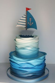 a three tiered cake with a sailboat on top and blue waves around it