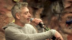 a man singing into a microphone with graffiti on the wall behind him