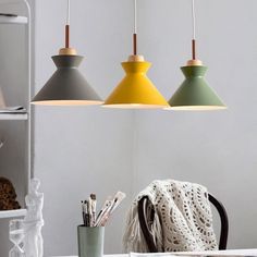 three different colored lamps hanging over a table with pens and pencils in front of it