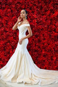 a woman in a wedding dress standing next to a red rose wall with her hand on her cheek