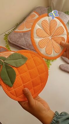 someone is holding an orange on top of a table next to some pillows and other items