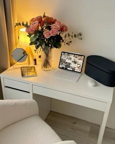 a laptop computer sitting on top of a white desk next to a vase with flowers