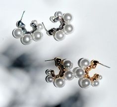 three pairs of pearl and diamond earrings on a white surface with black spots in the background