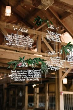 wedding seating chart hanging from the ceiling in a barn with greenery on it's sides