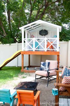 an outdoor play area with chairs and a slide in the back yard, next to a white fence