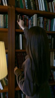 a woman standing in front of a bookshelf with a lamp on top of it