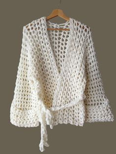 a white crocheted cardigan sweater hanging on a hanger with a wooden hanger