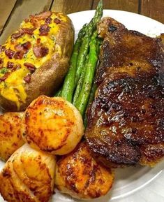 a white plate topped with steak, potatoes and asparagus next to a baked potato