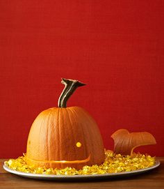 an orange pumpkin on a white plate with yellow corn in front of it and a red wall behind it